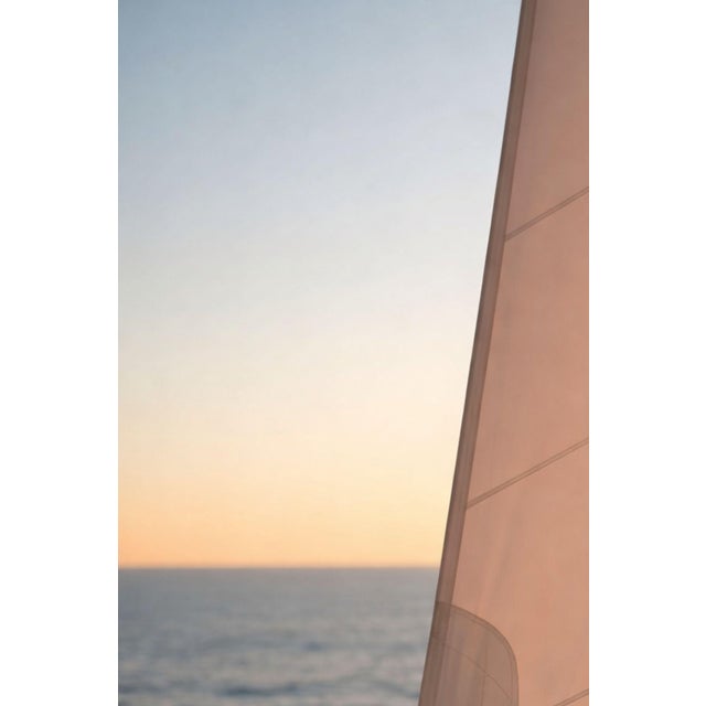 Minimalist coastal artwork featuring a sunlit sail against open water with soft golden tones and clean lines. The...