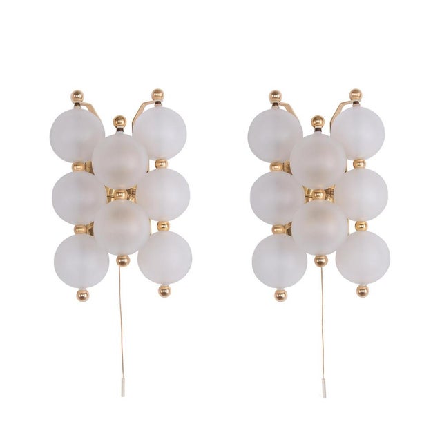 Elegant pair of wall lights with frosted glass balls with golden knobs on a brass frame. The lights illuminate...