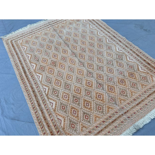 This hand-knotted Taimani rug showcases an allover diamond lattice in soft camel and ivory, accented with small rust-red...