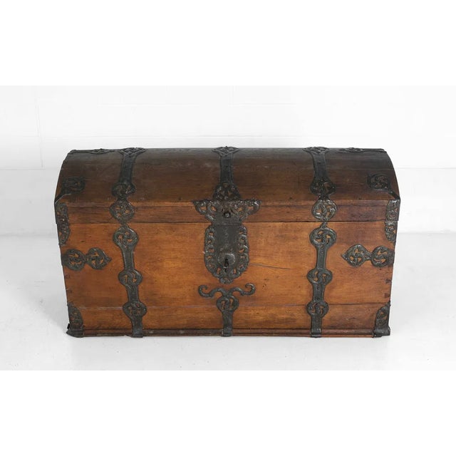 A commanding dome-top coffer in oak, bound front and lid with hand-wrought iron strapwork in scrolling foliate forms. The...