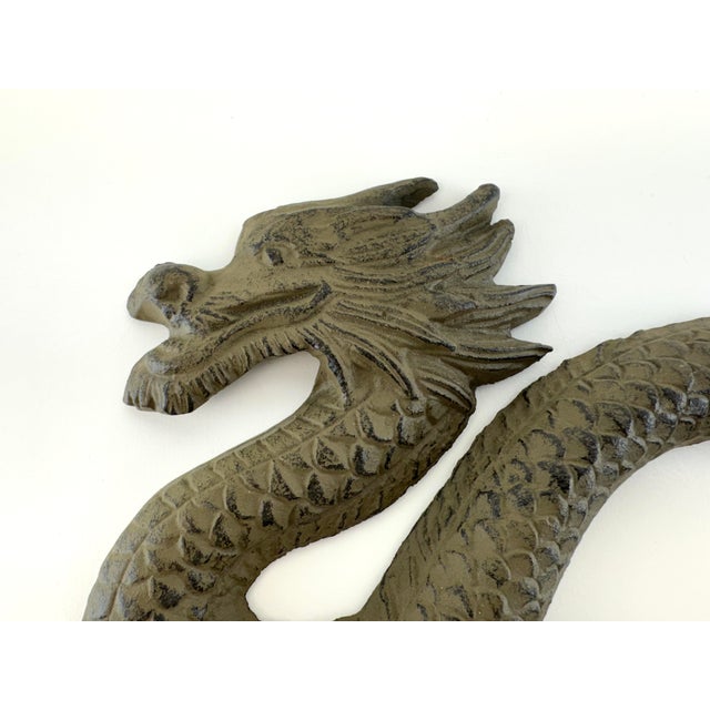 A striking vintage cast iron wall hook featuring a sinuous dragon in high relief, its scaled body winding across a cloud-...