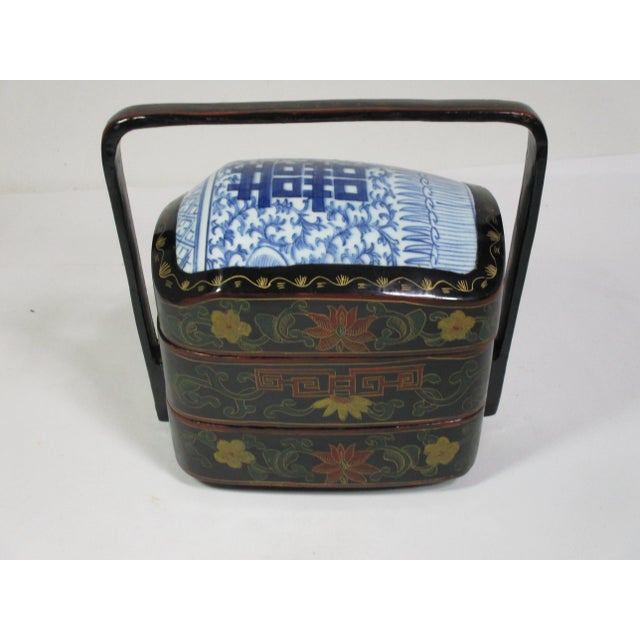 A vintage Chinese handmade and hand painted two-tiered black lacquered stacking box with handle. It has an antique double...