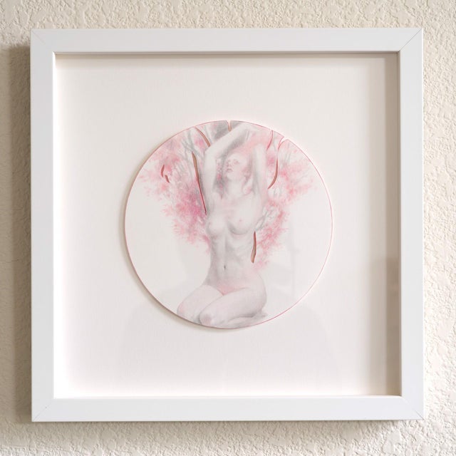 The artwork features a nude figure in a seated pose, gracefully arching her back against a backdrop of soft, pink foliage....