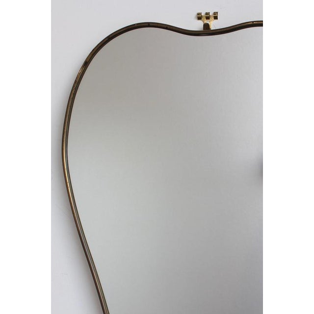 Mid-century italian wall mirror with brass frame (circa 1960s). The mirror is uniquely-shaped, reminiscent of an apple,...