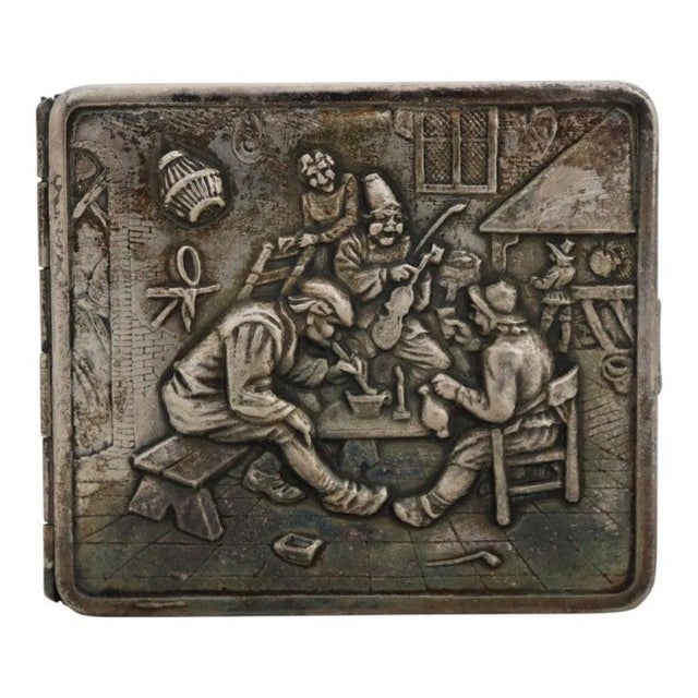 This antique sterling silver cigarette case, dating to approximately 1900, features an intricately repoussé figural scene...