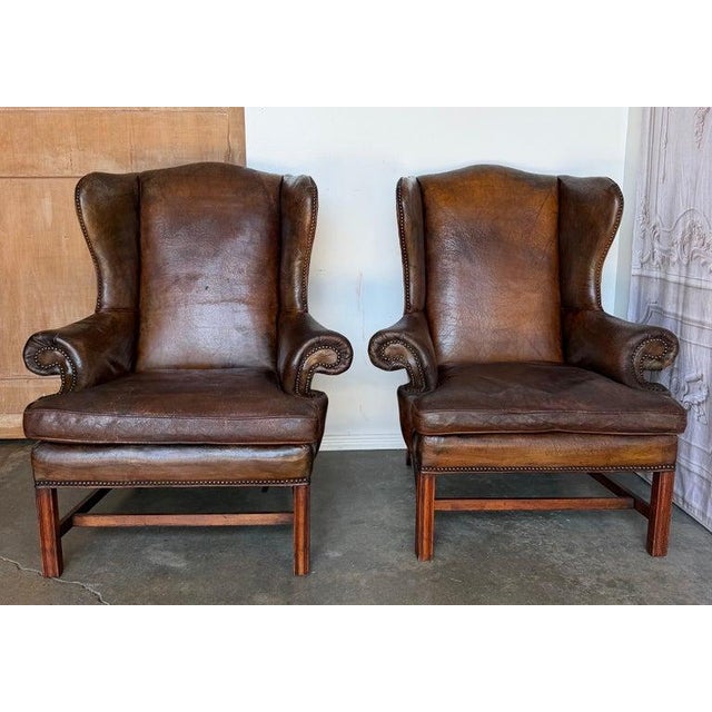 A magnificent pair of Georgian-style wingback armchairs, executed in the timeless tradition of the English Chesterfield...