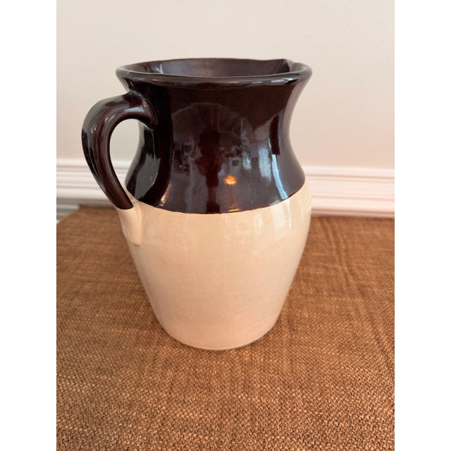 Charming vintage two-tone stoneware pitcher featuring a rich chocolate brown glazed upper body over warm cream pottery...