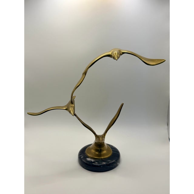 Striking mid-century modern brass sculpture featuring three seagulls in flight mounted on a polished black marble base....
