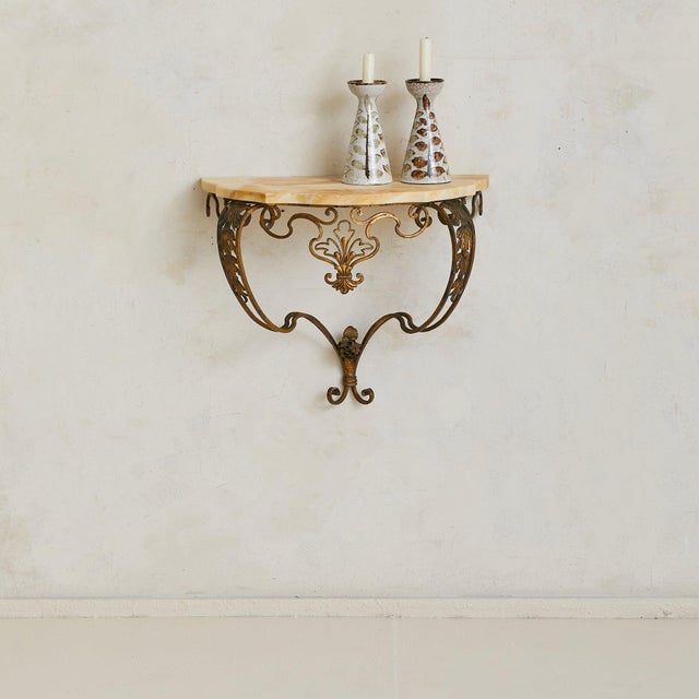 A petite French brass and marble wall-mounted console, dating to the 1940s. Shaped in scrolling wrought brass, the frame...