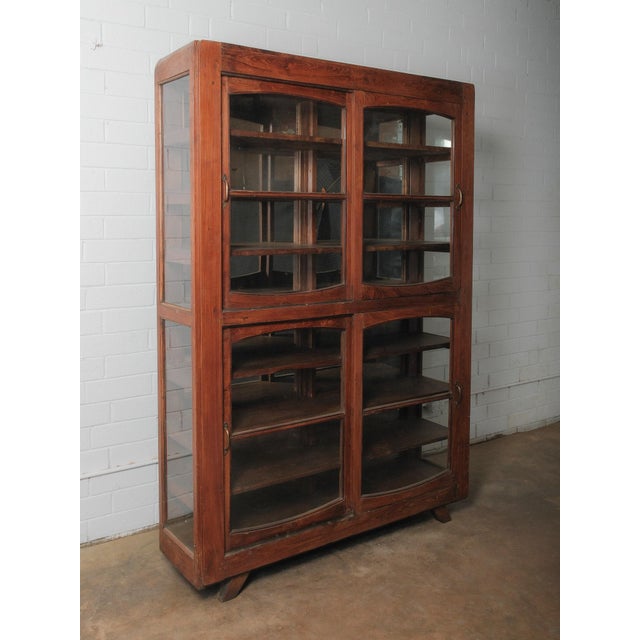 A commanding wooden display cabinet defined by its sculptural arched-glass doors and warm, time-worn finish. The tall,...