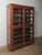 A commanding wooden display cabinet defined by its sculptural arched-glass doors and warm, time-worn finish. The tall,...