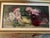 The composition features a lush arrangement of chrysanthemums and dahlia-like blossoms overflowing from a classical...