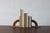 A pair of wooden bookends with a distinctive, architectural design. Each is built on a rectangular base. Between them is a...