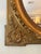 This mirror is within a square frame and oval cutout with foliate trim in a satin and burnished finish. At each corner are...