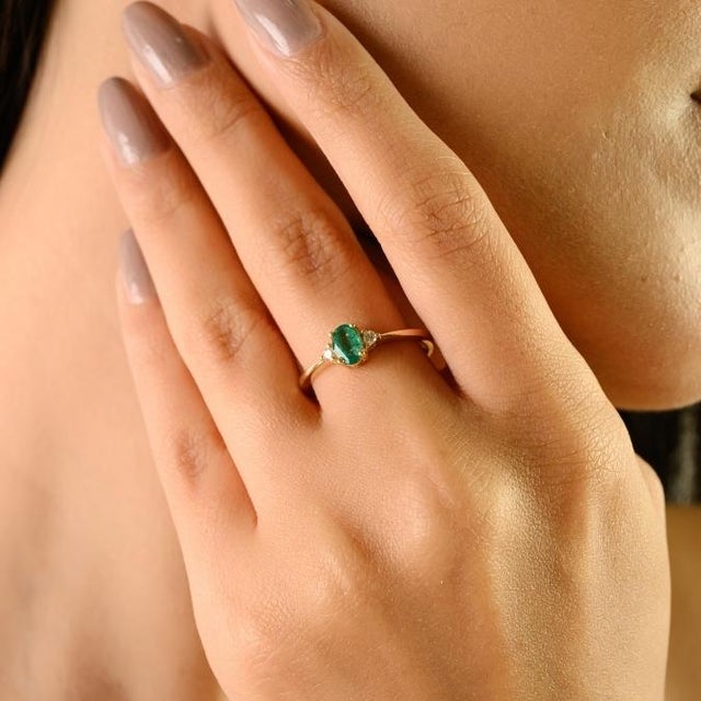 This minimalist three-stone ring showcases a natural oval-cut emerald weighing approximately 0.37 carats, set in solid 14K...