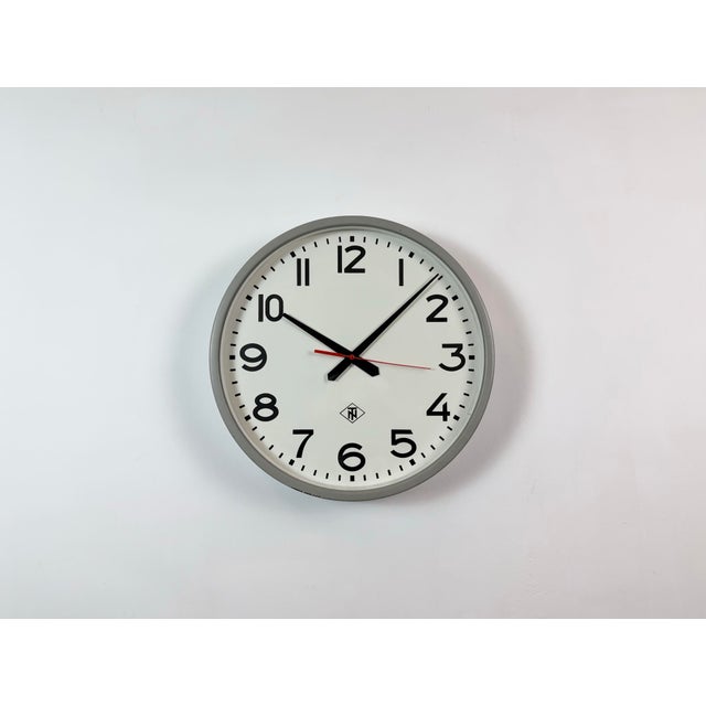 Wall clock produced by TN Telefonbau und Normalzeit in Germany during the 1960s. It features a grey iron frame, a white...