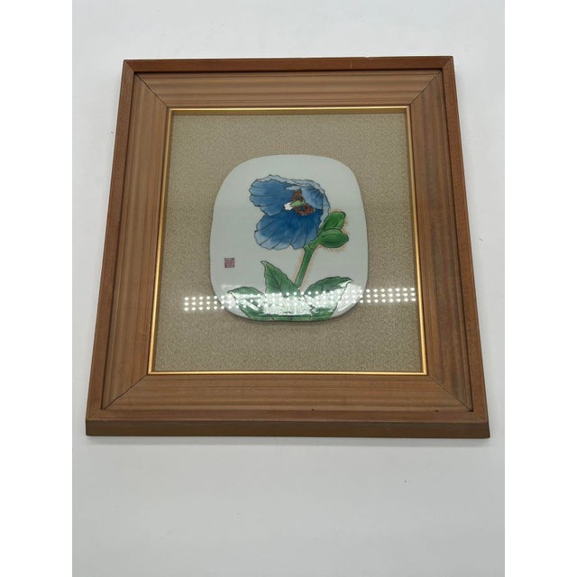 A refined Japanese decorative wall art piece featuring an oval porcelain plaque adorned with a vivid blue floral design....
