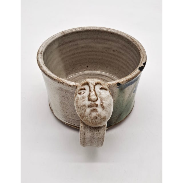 A one-of-a-kind matched pair of hand-thrown, wide-mouth stoneware mugs, each topped with its own sculpted face medallion...