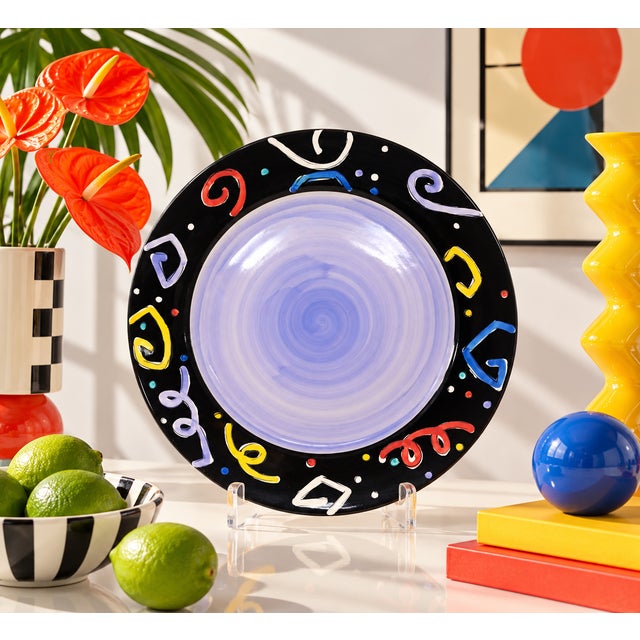A 13 1/4" diameter ceramic platter, hand-painted with a purple center and postmodern-style designs around the border. Good...