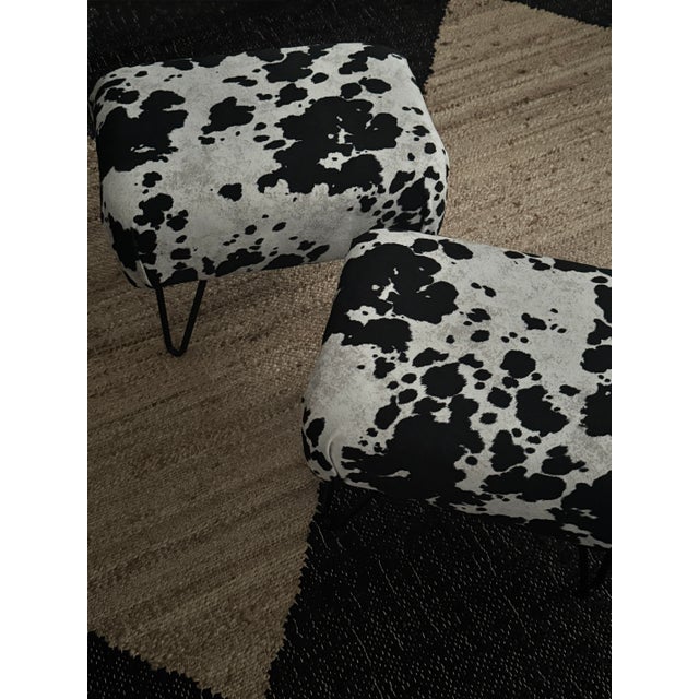 A sculptural pair of late 20th-century stools upholstered in black-and-white cowhide, set on slender black hairpin legs....