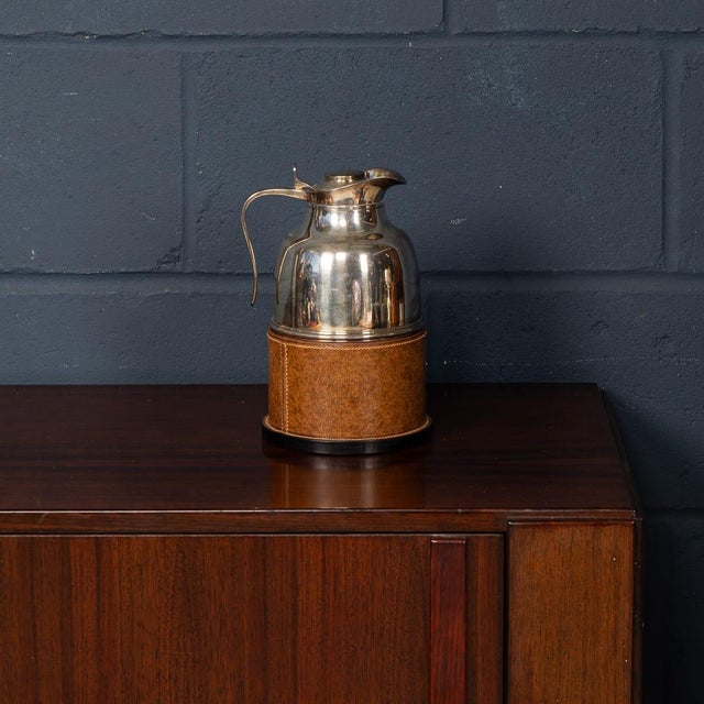 This elegant hot water flask features a silver-plated vessel housed in its original leather sleeve, offering both...
