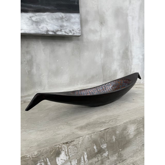 A striking and sculptural hand-carved vessel in richly toned mango wood, measuring an impressive 95 cm in length. Its...