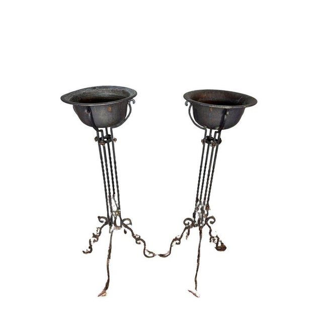 Pair of antique wrought iron plant stands, each retaining its fitted pot. Hand-forged with elegant scrollwork and a rich,...