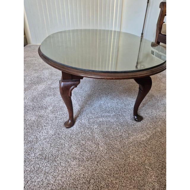 This is a classic Queen Anne style oval coffee table. It is crafted from a rich, warm hardwood—typically cherry or...