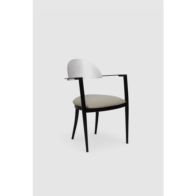 Set of four minimalist dining chairs defined by curved stainless steel backrests and two tone black metal frames. A...