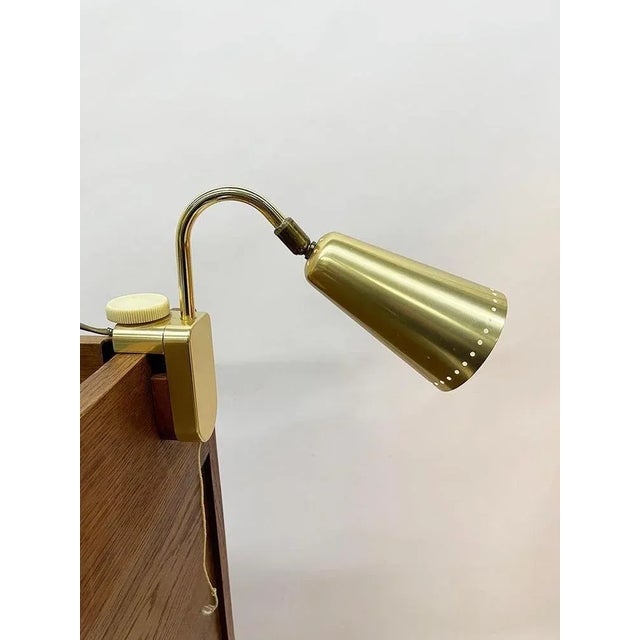 A german reading lamp with adjustable bracket in a brass-colored aluminum conical shaped lampshade, perforated with small...