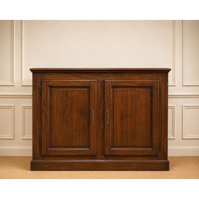 A low Regency-style sideboard with two doors, crafted from solid oak with a dark brown stain, resting on a wide, molded...