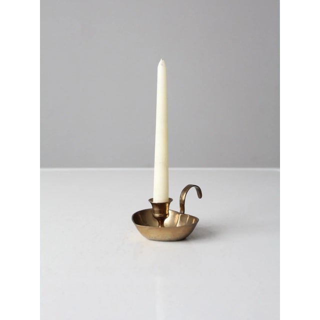A charming vintage brass chamberstick with a distinctive heart-shaped drip pan and open handle. The warm brass finish and...