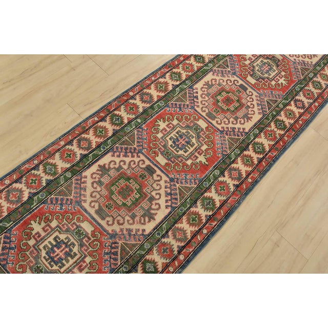 A tribal Caucasian Kazak runner hand-knotted with fine wool on a cotton foundation. This rug features a row of geometric...
