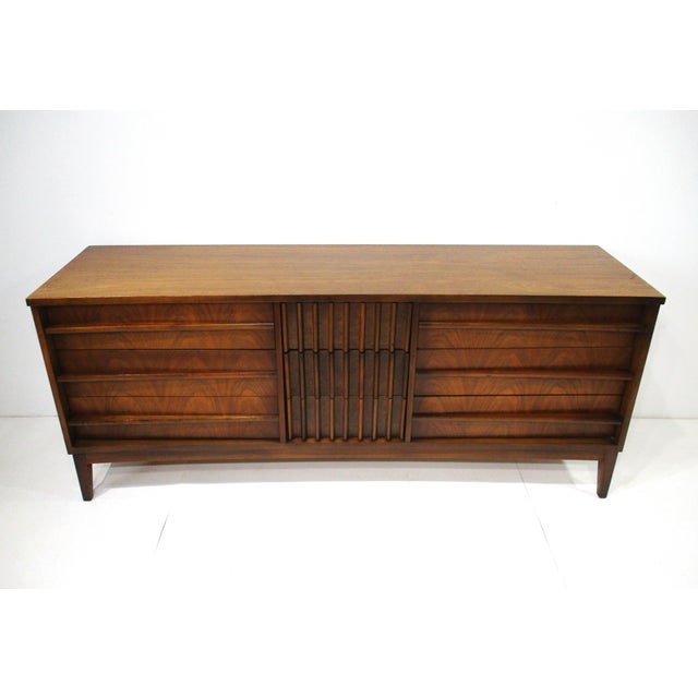 A mid-century walnut low boy dresser with nine drawers perfect for your storage needs with the three center drawers having...