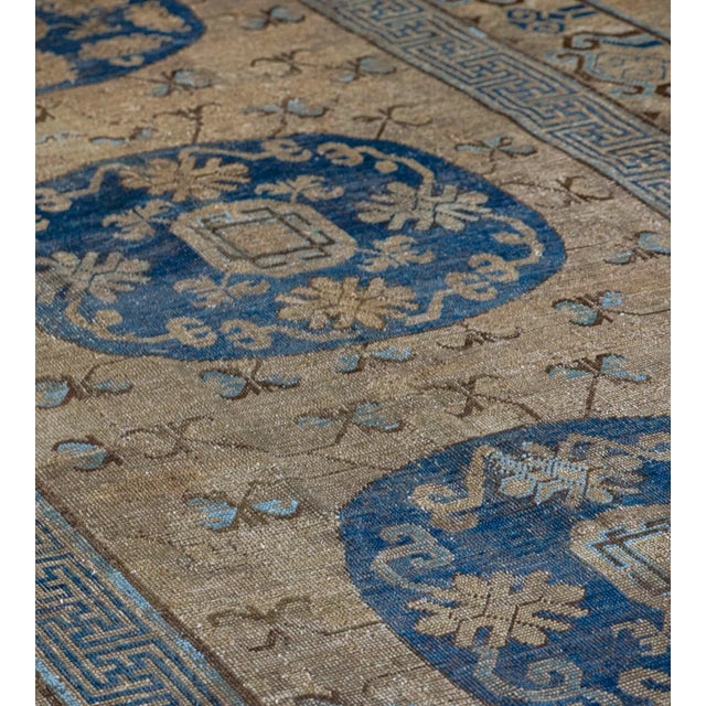 This antique Khotan rug has a dusty sandy-brown field scattered with delicate light blue and golden-yellow delicate...