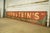 Reclaimed movie set sign made of aluminum in red, green, and white colors. The sign reads "145, Bernstein's, Woolens &...