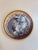This circular oil painting on birch panel captures a serene moment of a cat curled up in a cozy nest. The soft, textured...