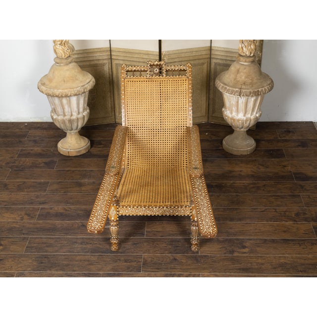 An Anglo-Indian wood and cane plantation chair from the early 20th century, with foliage-themed bone inlay and extending...