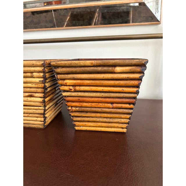 A pair of tapered square cachepots made of stacked bamboo reeds, laid horizontally around a wood frame, with the reed ends...