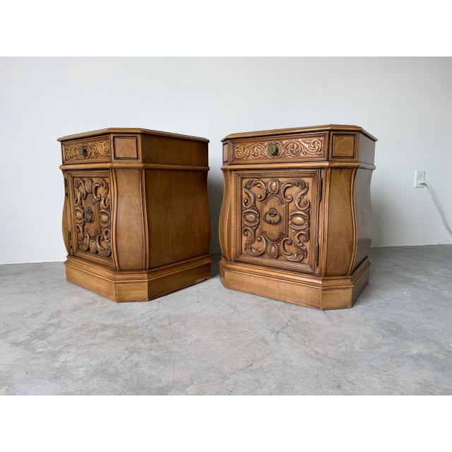 Beautiful pair of vintage Hollywood Regency style nightstands featuring richly carved cabinet doors with ornate scrollwork...