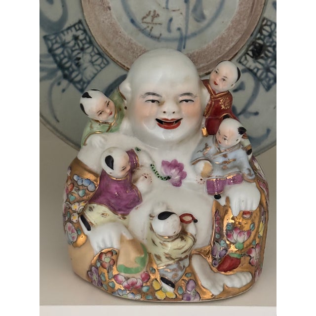 This vintage Chinoiserie style porcelain figure of Budai, the Laughing Buddha is seated and surrounded by five playful...