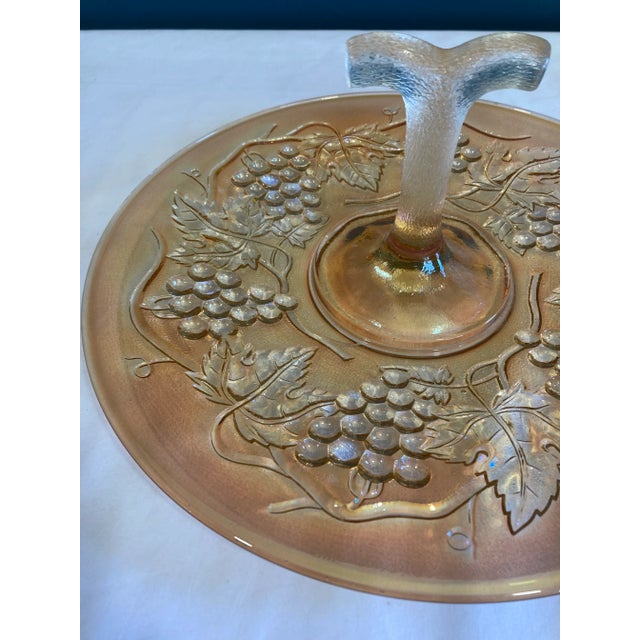 This vintage orange iridescent glass cake plate features beautiful etched grape detailing and a charming central handle...
