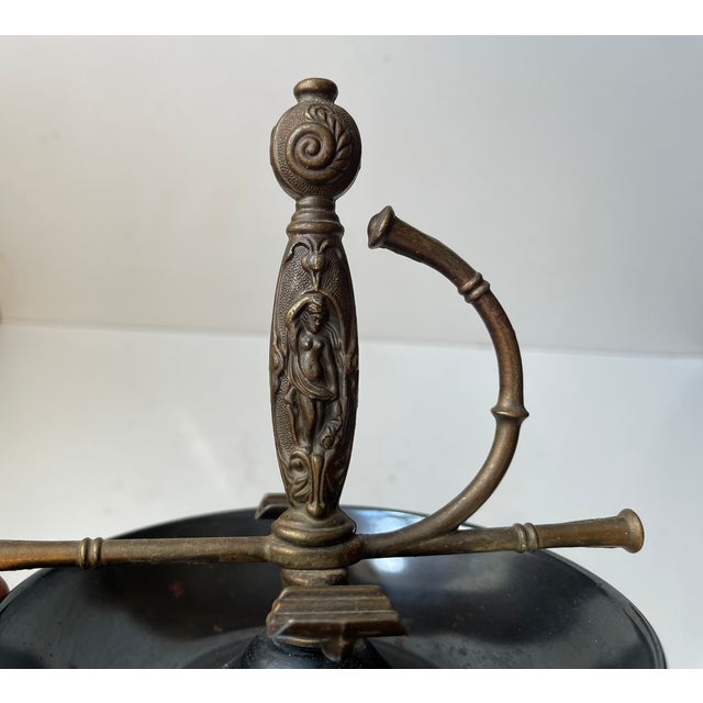 A Spanish made unusual ashtray in sculpted brass and black/dark grey lacquered metal. Its center sword handle that holds...