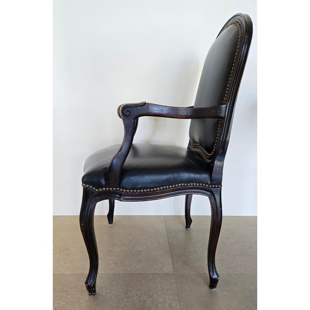 Pair of carved walnut frame arm chairs with black leather and brass nail head trim. Some age wear to leather and wood. The...
