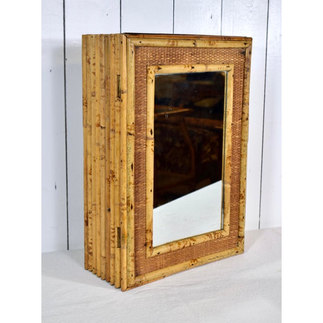 A delightful vintage tortoise bamboo single door wall cabinet with mirror, accented with grass cloth surround and one...