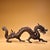 This is a cast bronze figurine of a walking dragon, featuring a gilded finish with a dark, aged patina. The dragon is...