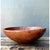 This large wooden bowl is carved from a single piece of solid wood, its rounded, gently asymmetrical form bearing the...