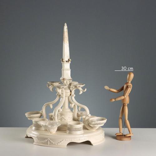 Earthenware centerpiece set on a circular base embellished with relief festoons. A central obelisk supported by four lions...