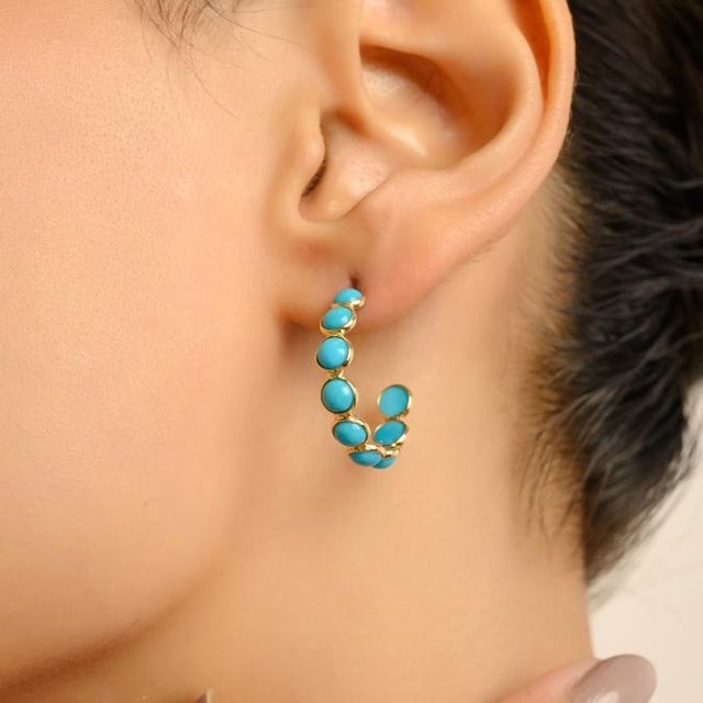 These elegant hoop earrings are crafted in 18K yellow gold, showcasing round cabochon-cut turquoise gemstones with a total...