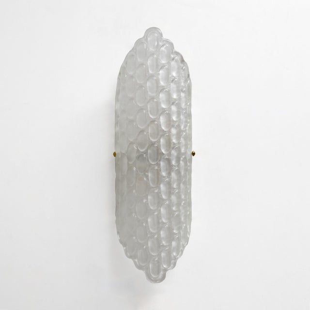 Elegant pair of wall sconces featuring large diffusers in clear Murano glass, handcrafted with a refined relief surface...